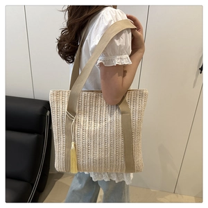 Detail of woven straw tote bag with brown straps and yellow tassel on shoulder