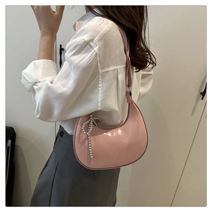 Pink patent leather half-moon shoulder bag with pearl bow charm detail on model