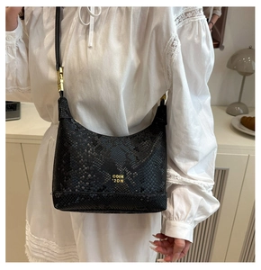 Close-up of black snake-embossed leather tote with gold logo and crossbody strap detail