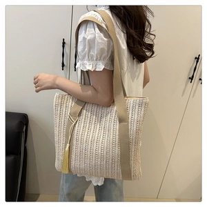 Detail of woven straw tote bag with khaki straps and yellow tassel on shoulder