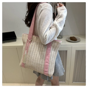 Detail of woven straw tote bag with pink canvas straps and decorative cotton tassel