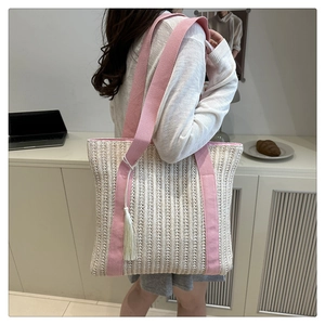 Detail view of woven straw tote bag with pink shoulder strap and white tassel on a model