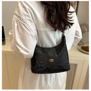 Détail d'un sac à bandoulière noir effet serpent avec logo doré porté par un mannequin