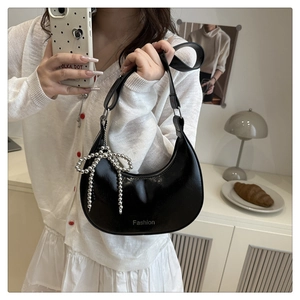 Detail of black glossy hobo bag featuring a silver bow charm and Fashion logo