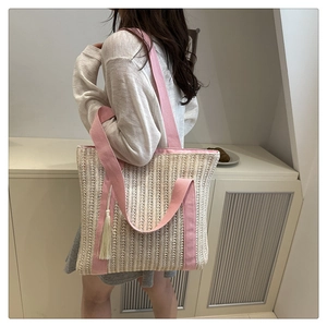 Detailed close-up of a woven straw tote bag featuring pink wide straps and tassel detail