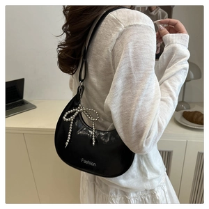 Detail of black patent leather crescent bag with silver Fashion print and bow charm