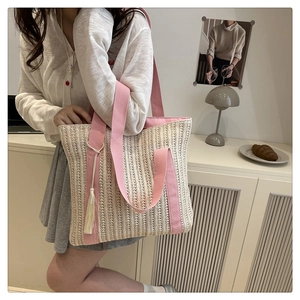 Detail of hollow straw tote bag with pink canvas straps and beige fringe charm