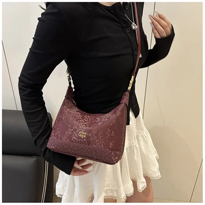 Detail of burgundy crocodile pattern crescent bag with gold logo and hardware accents