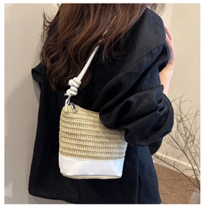 Detail of woven straw bucket bag with white leather base and knotted shoulder strap
