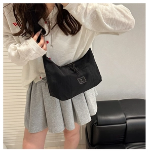 Close-up of minimalist black nylon crossbody bag with square logo patch worn by model