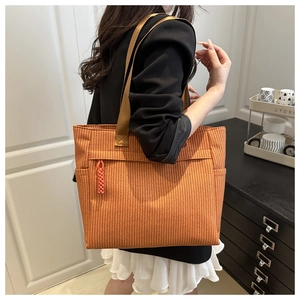 Detail of a large orange woven tote bag showing the side view and shoulder strap on a model