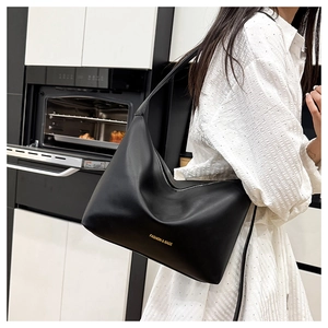 Detailed close-up of a minimalist black leather tote bag with gold lettering on a shoulder