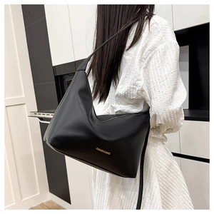 Detail of a minimalist black leather tote bag with gold lettering shown on a model