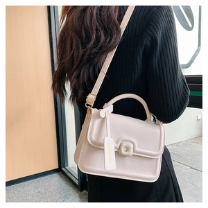 Detail of cream crossbody bag with leather texture and decorative fashion tag