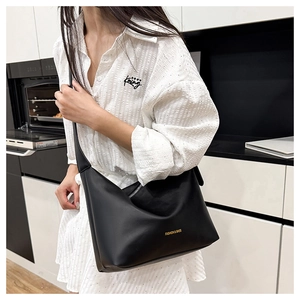 Close-up of minimalist black hobo bag with gold text detail and stylish white shirt