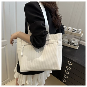 Close-up of white woven tote bag with wide shoulder strap and functional zippers