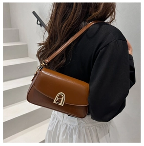 Sac à bandoulière vintage marron avec boucle dorée arquée porté par un mannequin en extérieur