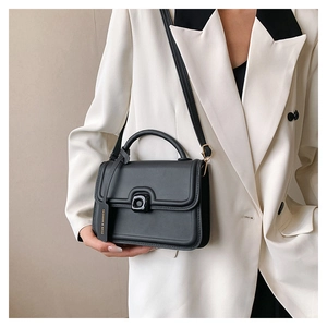 Detail of a matte black square bag with a structured frame and matching logo tag