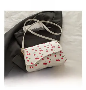 Close-up of white shoulder bag with red cherry print compared to a black mobile phone