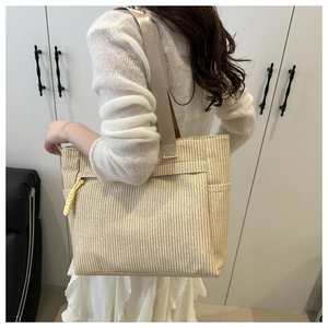 Detailed back view of a beige woven tote bag with wide strap and yellow rope pendant