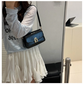 Sac bandoulière en cuir noir brillant avec boucle dorée porté par un mannequin