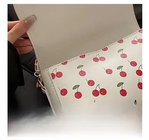 Detail view of the golden magnetic closure on a white shoulder bag with red cherry prints