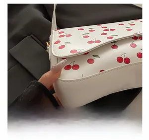 Close-up of white leather shoulder bag featuring cherry print and precise stitching details