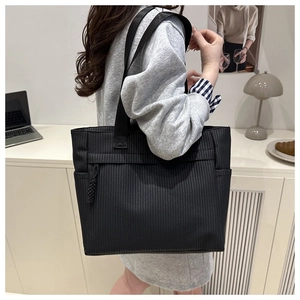 Close-up of black tote bag featuring vertical striped texture and side zipper detail