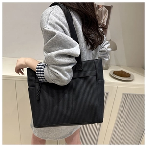 Detailed view of black pleated tote bag with vertical stripes shown on model's shoulder