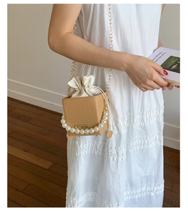 Detail of woven bucket bag with large pearl handle and golden chain strap on model