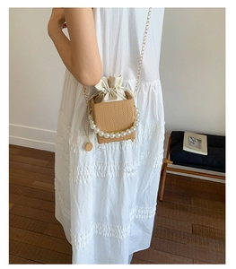 Detail of hand-woven straw bucket bag featuring a large pearl handle and a gold chain strap