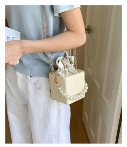 Chic beige woven bucket bag featuring pearl handle and gold chain strap shown on model