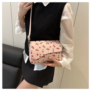 Detailed view of pink shoulder bag featuring red cherry prints and wavy flap edge