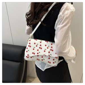 Side view of white crossbody bag featuring red cherry prints and adjustable shoulder strap