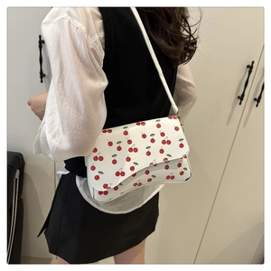 Detail shot of a white crossbody bag with red cherry prints worn by a model in soft light