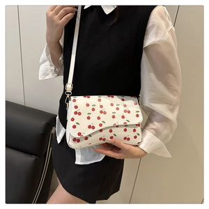 Detail of white crossbody bag with cherry prints and asymmetrical curved flap design