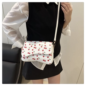 Detailed view of white crossbody bag with red cherry print worn by a fashion model