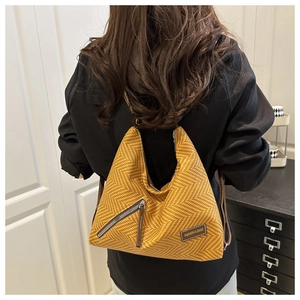 Detalle del bolso bandolera de tejido espiga amarillo con parche de cuero y logo de moda