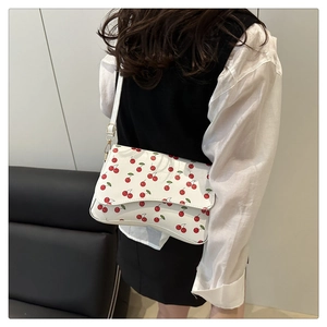 Close-up of white shoulder bag featuring red cherry prints and golden buckle detail