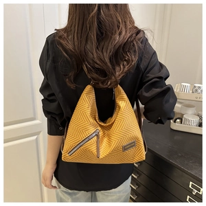 Close-up of yellow woven tote bag featuring metal zipper and brand leather patch detail