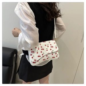 Detailed view of the cherry print pattern and gold buckle on a white leather crescent bag