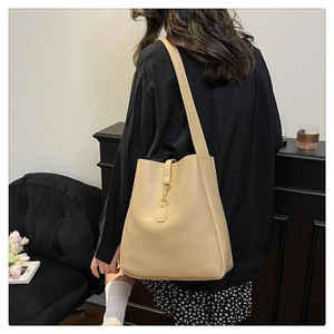 Detail of beige bucket bag with gold hook closure and matching wide strap on model