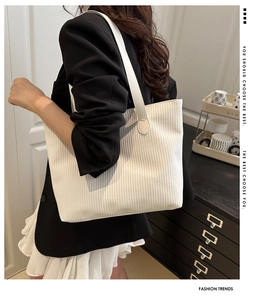 Detail of white striped tote bag with leather straps on model wearing a black blazer