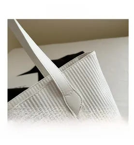 Detail shot of white woven tote bag showing fine texture and reinforced leather handle attachment