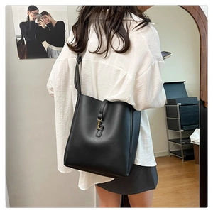 Side view of a large black leather bucket bag with gold clasp shown on model