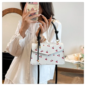 Close-up of a white cherry print handbag with black knotted handles and gold metal rings