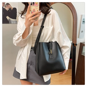 Detailed view of black bucket bag with gold clasp shown on a model for scale and style