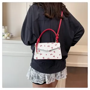 Detailed view of white cherry print handbag featuring red handles and V-shaped clasp