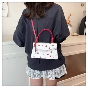 Detail of sweet cherry print crossbody bag with red round handles on white leather