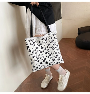 Close-up of white canvas tote bag with black floral print and delicate lace trim detail